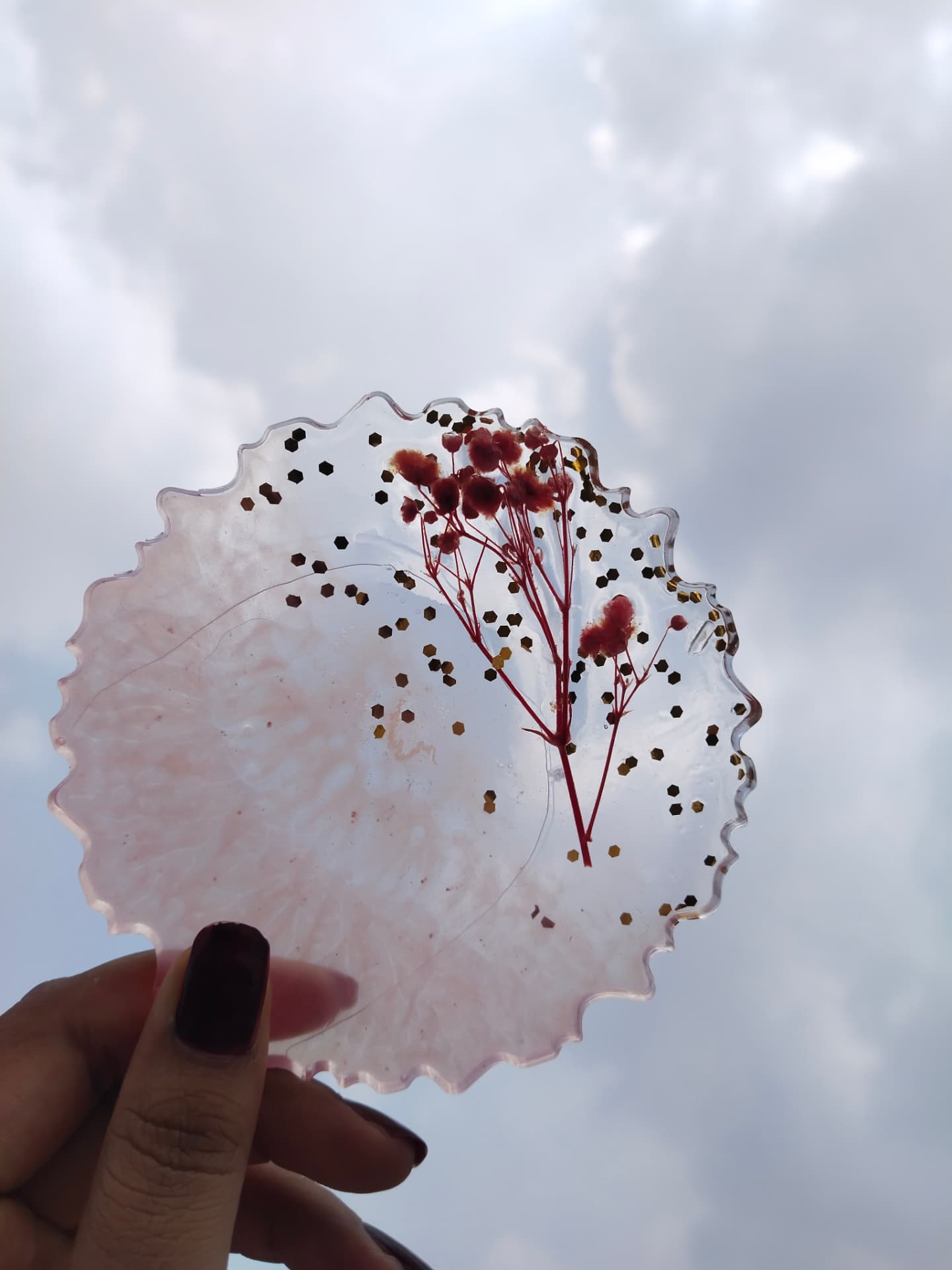 Blush resin piece with dried red flowers and gold flakes held against the sky